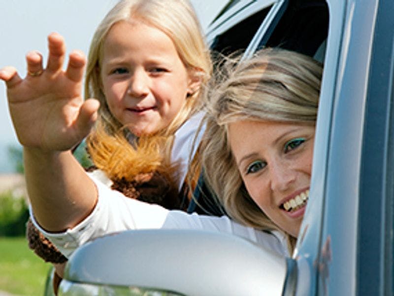 Vrouw in auto met kind, beide hangen half uit het raam 